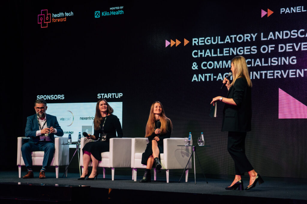 Panelists on stage at Health Tech Forward discussing regulatory challenges in developing and commercializing health technologies, with event branding displayed behind them.
